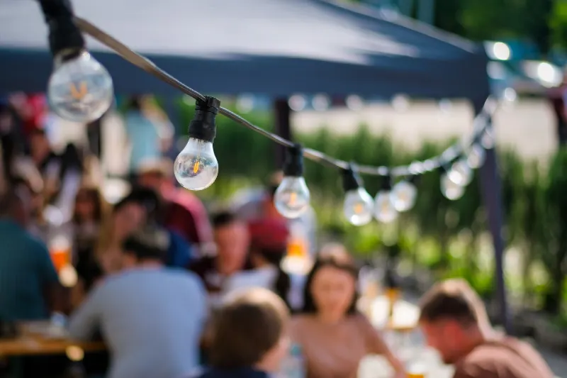 Lampjes boven een buitenfeest, met mensen aan tafel op de achtergrond